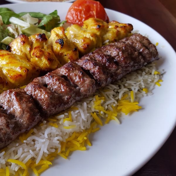 Persian kabob plate with grilled beef koobideh, chicken, saffron rice, roasted tomato, and salad.