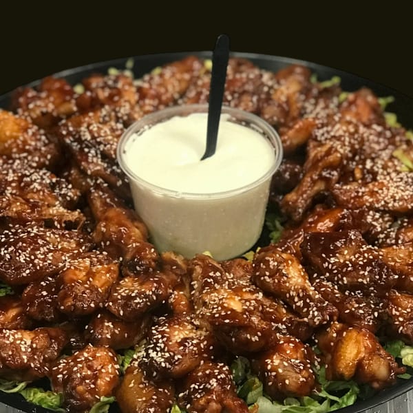 A platter of sesame chicken wings with a side of creamy white dipping sauce and lettuce.