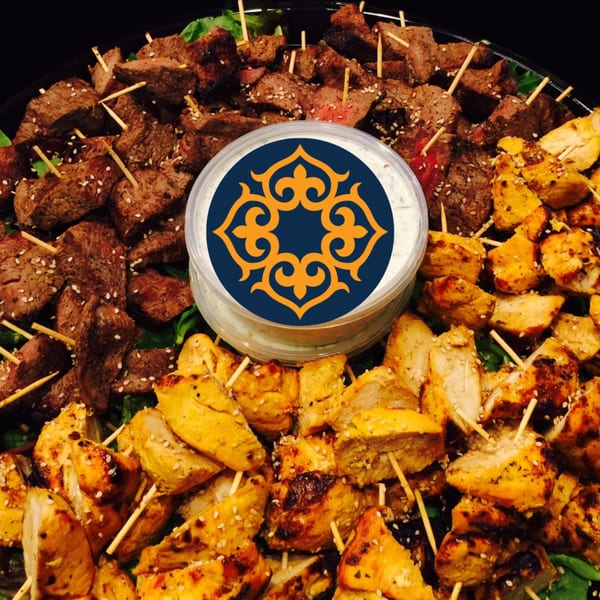 A platter of beef and chicken skewers with sesame seeds, and a dipping sauce in the center.