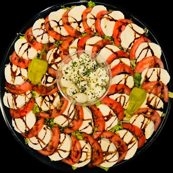 Caprese salad platter with sliced tomatoes, mozzarella, balsamic glaze, and a center of mozzarella balls.