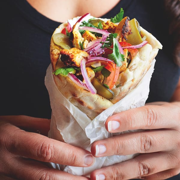 Hands holding a BÖRO KABOB wrap filled with chicken, red onions, tomatoes, and pickles.