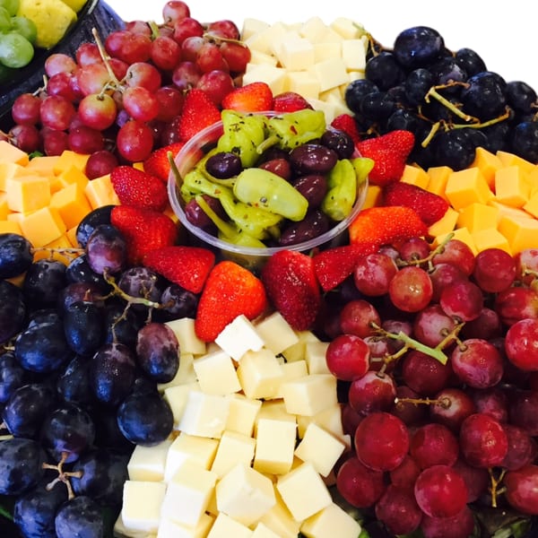 A colorful platter of red and green grapes, strawberries, cheese cubes, and pickled peppers.