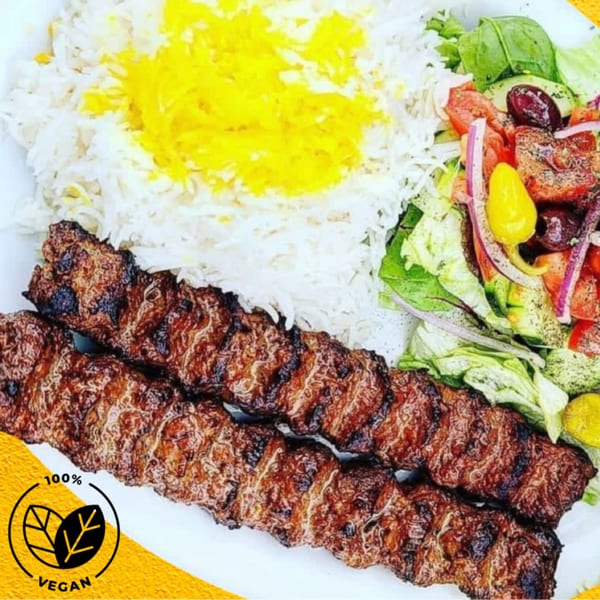 Two skewers of grilled kabob, white rice with saffron, and a fresh salad with olives.