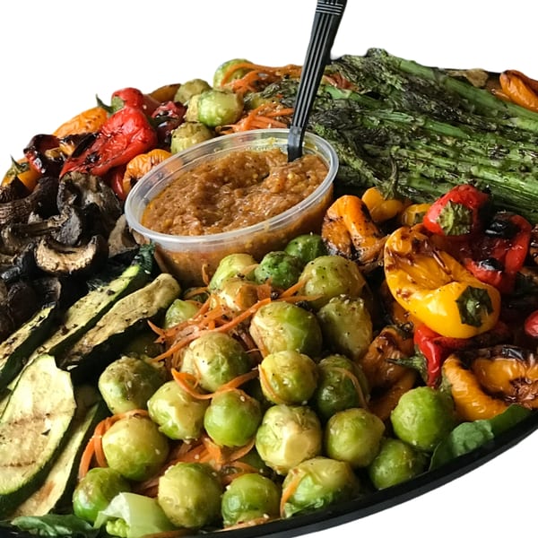 A platter of grilled vegetables, including asparagus, bell peppers, zucchini, mushrooms, and Brussels sprouts with a dipping sauce.