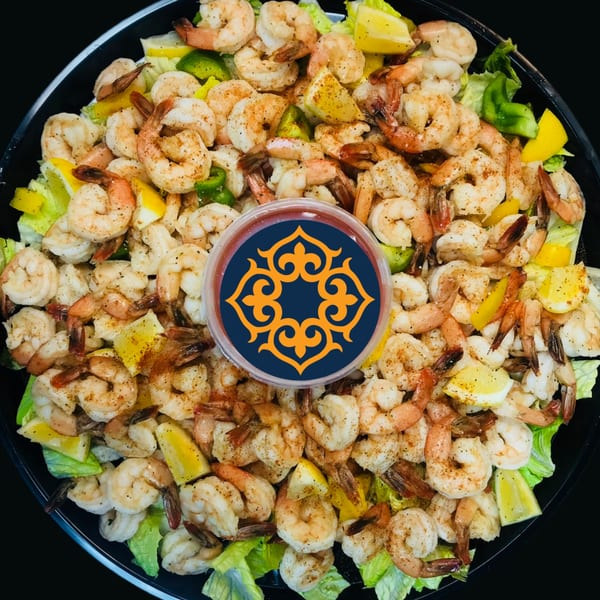 A large platter of seasoned shrimp with lettuce, lemon wedges, and a dipping sauce in the center.