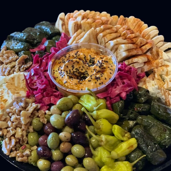 A platter of hummus, pita bread, stuffed grape leaves, olives, pickled peppers, walnuts, and red cabbage.